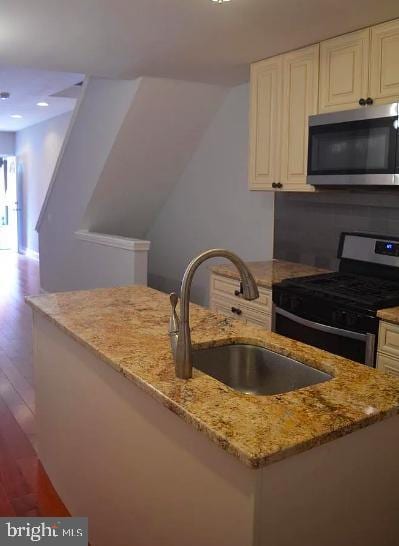 kitchen featuring light stone countertops, sink, light hardwood / wood-style flooring, and appliances with stainless steel finishes