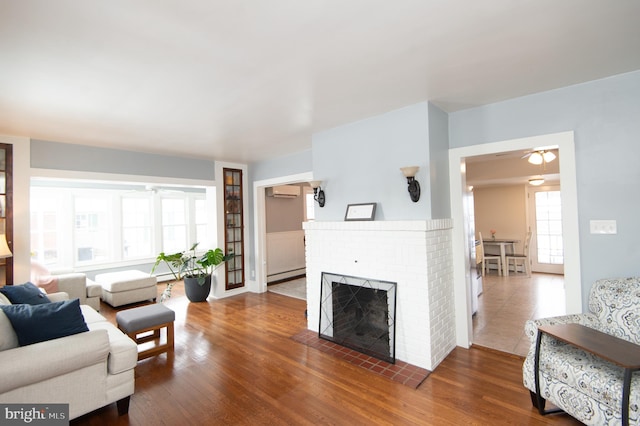 living room featuring an AC wall unit, a brick fireplace, baseboard heating, and dark wood-type flooring