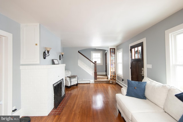 living room featuring a brick fireplace, dark wood-type flooring, and a baseboard heating unit