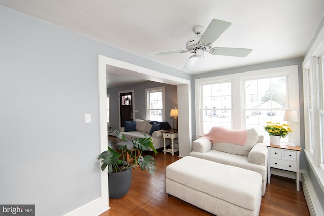 living area with dark hardwood / wood-style floors, baseboard heating, and ceiling fan