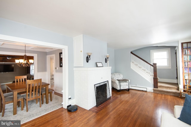 living room with a brick fireplace, an inviting chandelier, dark wood-type flooring, and a baseboard radiator