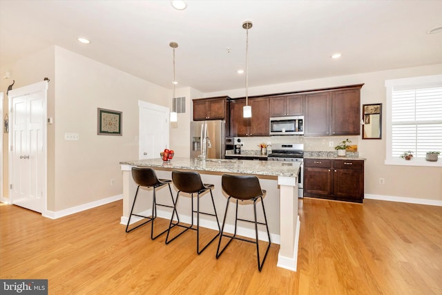 kitchen featuring a center island with sink, a kitchen breakfast bar, light hardwood / wood-style flooring, decorative light fixtures, and stainless steel appliances