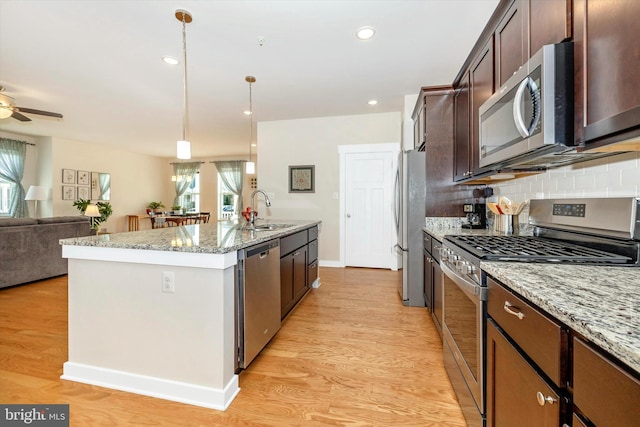 kitchen with decorative light fixtures, sink, light stone countertops, and stainless steel appliances