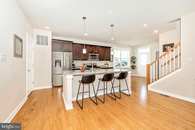 kitchen featuring a kitchen breakfast bar, an island with sink, appliances with stainless steel finishes, dark brown cabinets, and light stone counters