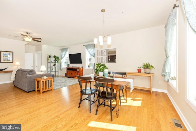 dining room with ceiling fan with notable chandelier and light hardwood / wood-style floors