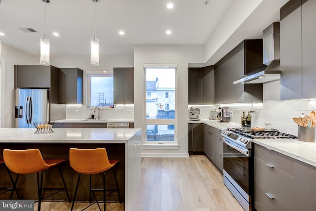 kitchen featuring a kitchen breakfast bar, wall chimney range hood, sink, gray cabinets, and appliances with stainless steel finishes