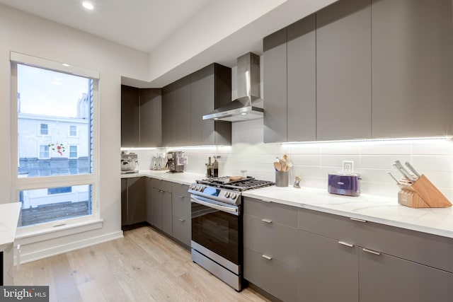 kitchen featuring gray cabinetry, gas stove, and wall chimney range hood