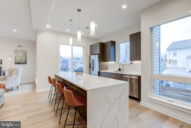 kitchen featuring light wood-type flooring, light stone counters, stainless steel appliances, a kitchen island, and hanging light fixtures