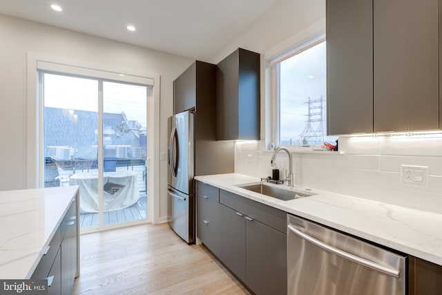 kitchen featuring decorative backsplash, appliances with stainless steel finishes, light wood-type flooring, light stone counters, and sink