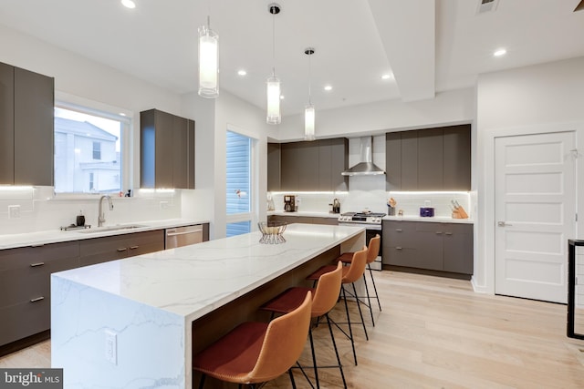 kitchen with appliances with stainless steel finishes, tasteful backsplash, sink, wall chimney range hood, and a kitchen island