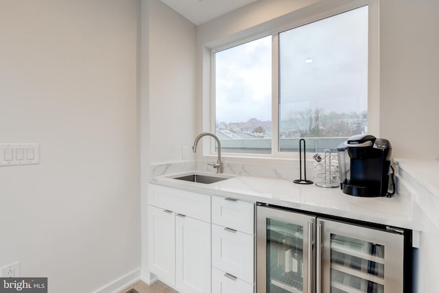 bar with light stone countertops, white cabinetry, sink, and beverage cooler