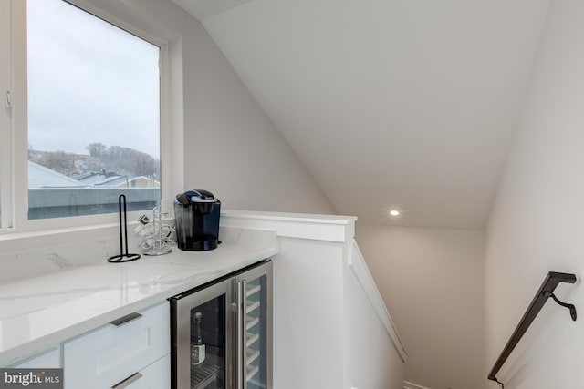 bar with wine cooler, white cabinetry, light stone countertops, and vaulted ceiling