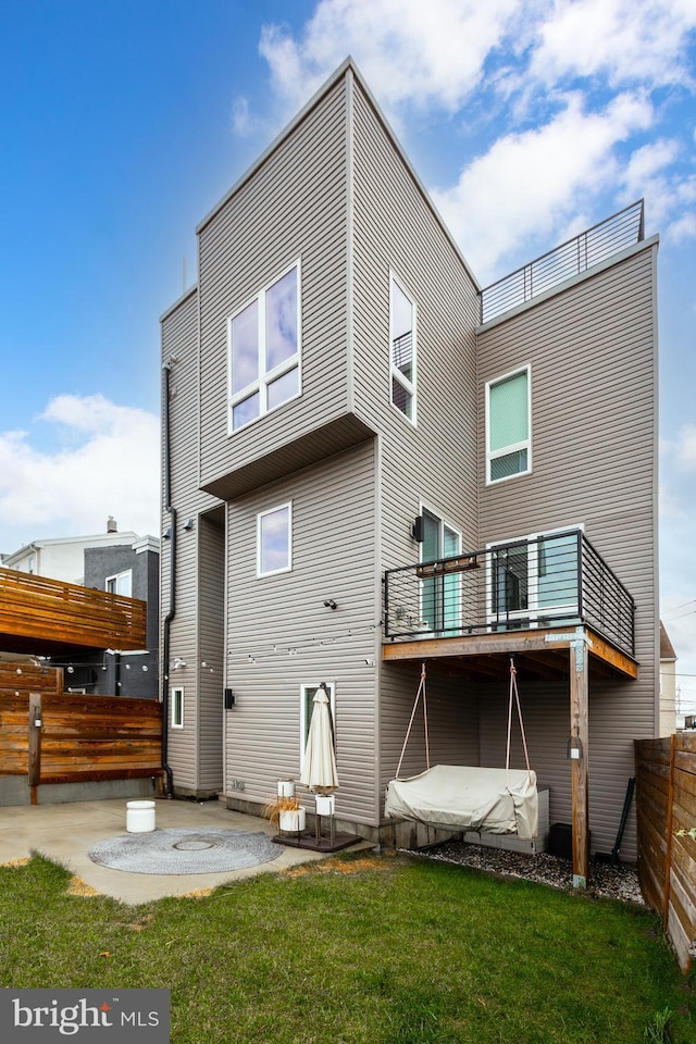 rear view of house with a balcony, a patio area, and a lawn