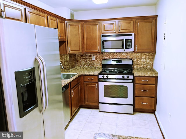 kitchen with backsplash, light stone counters, sink, and appliances with stainless steel finishes