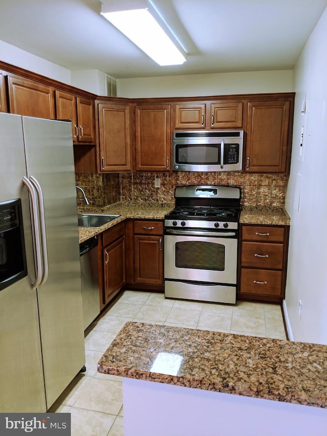 kitchen with sink, decorative backsplash, light tile patterned floors, appliances with stainless steel finishes, and stone countertops