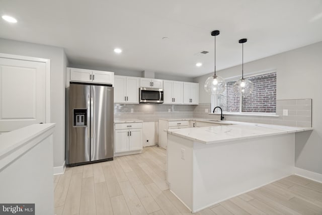 kitchen featuring kitchen peninsula, light stone counters, white cabinets, and appliances with stainless steel finishes