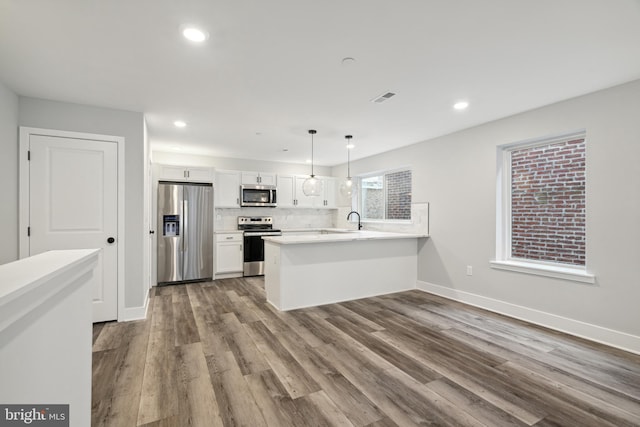 kitchen featuring white cabinetry, hanging light fixtures, stainless steel appliances, kitchen peninsula, and hardwood / wood-style floors