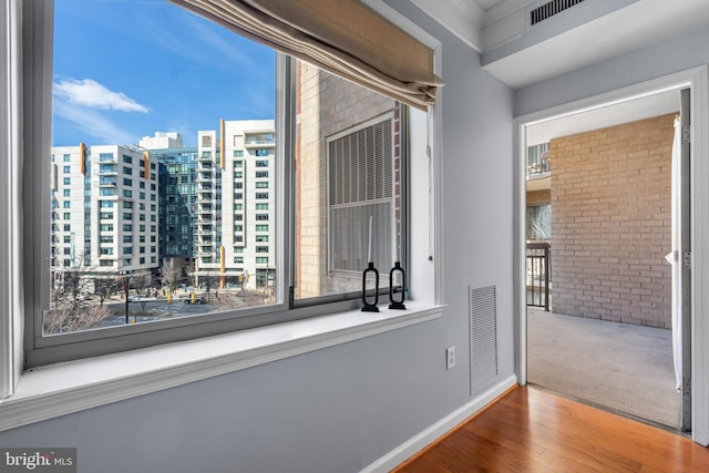 hallway featuring a city view, visible vents, brick wall, and wood finished floors