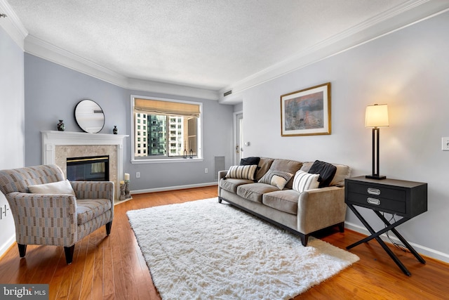 living area featuring a textured ceiling, a fireplace, baseboards, light wood-style floors, and crown molding