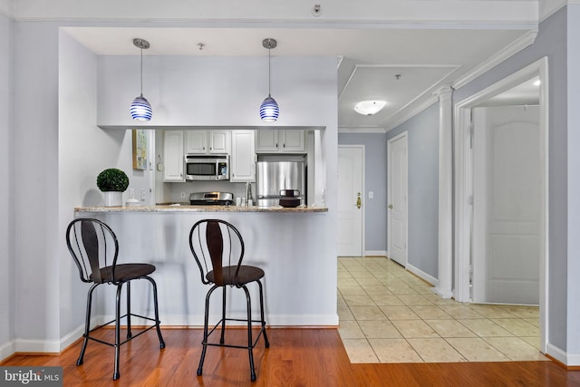 kitchen featuring ornamental molding, a kitchen breakfast bar, a peninsula, stainless steel appliances, and light tile patterned flooring