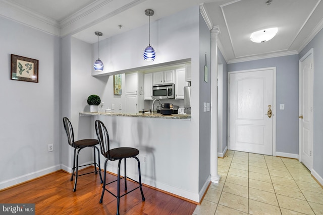 kitchen featuring stainless steel microwave, white cabinets, crown molding, and decorative light fixtures