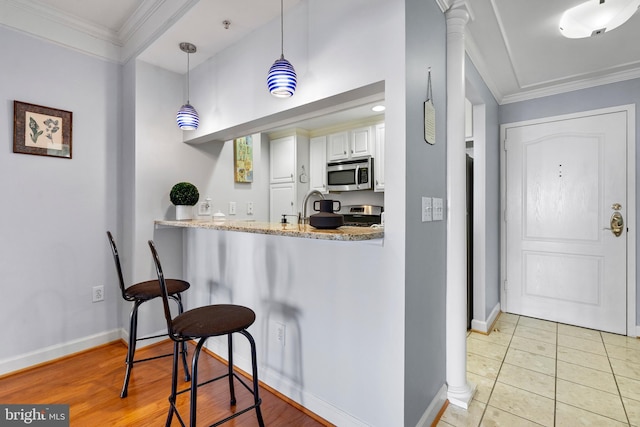 kitchen with stainless steel appliances, ornamental molding, a kitchen bar, and decorative columns