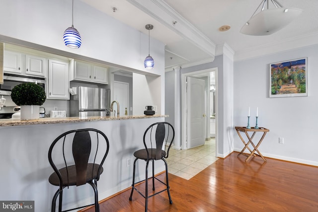 kitchen featuring a breakfast bar area, wood finished floors, appliances with stainless steel finishes, decorative light fixtures, and crown molding