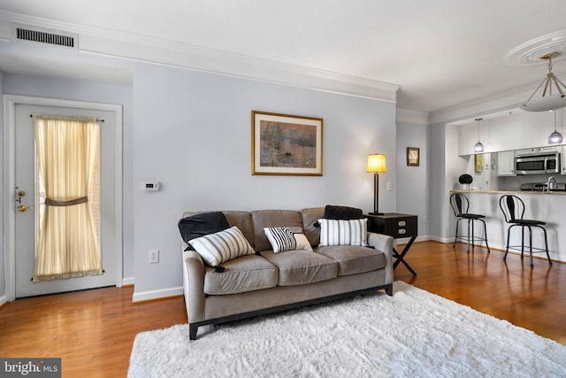 living area featuring visible vents, crown molding, baseboards, and wood finished floors