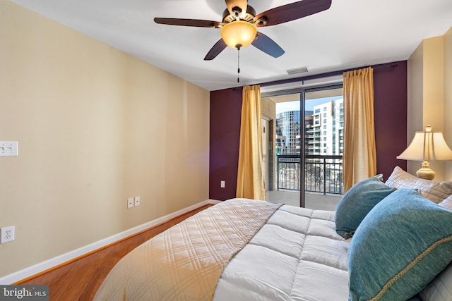 bedroom featuring baseboards, a ceiling fan, wood finished floors, access to exterior, and a wall of windows