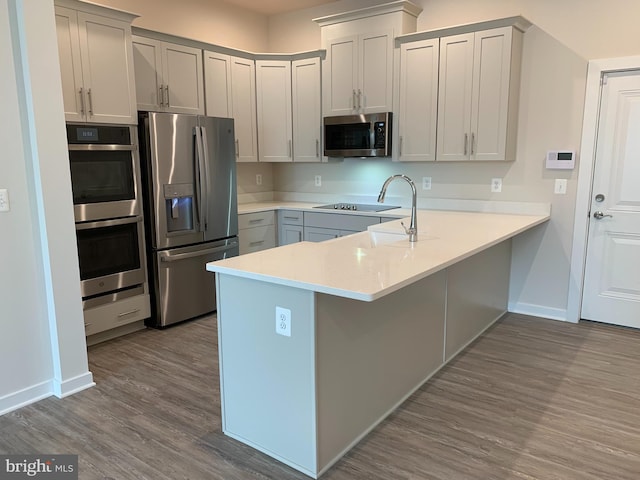 kitchen featuring stainless steel appliances, dark wood-type flooring, a peninsula, and light countertops