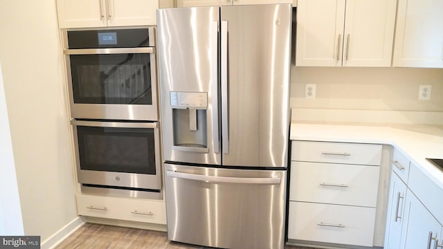 kitchen with light hardwood / wood-style floors, white cabinetry, and appliances with stainless steel finishes