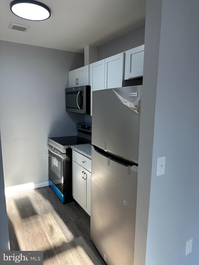 kitchen with stainless steel appliances, white cabinetry, and dark wood-type flooring