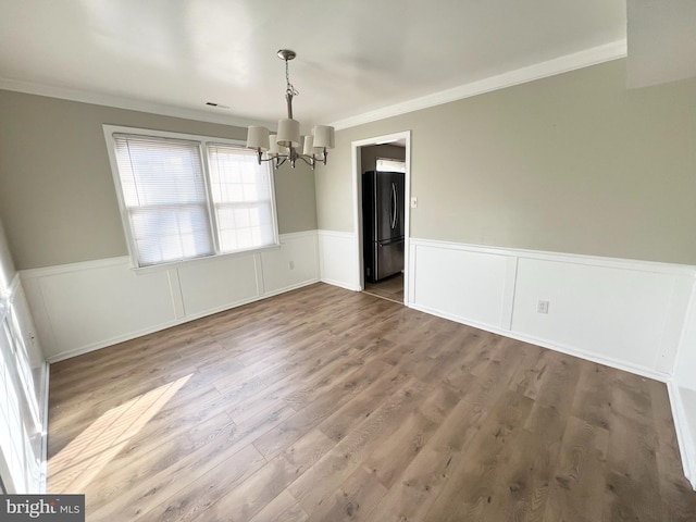 unfurnished dining area with wood-type flooring, an inviting chandelier, and crown molding