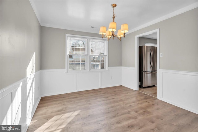 unfurnished dining area featuring light hardwood / wood-style floors, an inviting chandelier, and ornamental molding