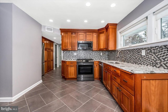 kitchen with light stone countertops, sink, stainless steel appliances, backsplash, and dark tile patterned flooring