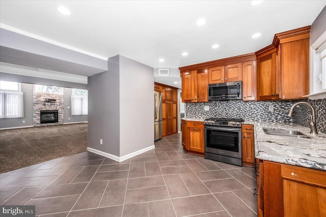 kitchen featuring dark carpet, sink, decorative backsplash, a fireplace, and appliances with stainless steel finishes