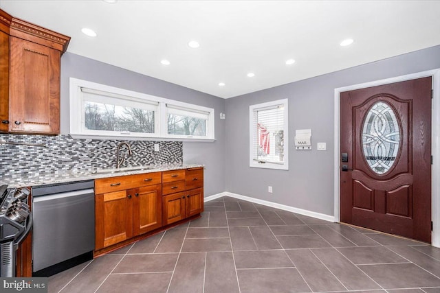 kitchen featuring sink, stainless steel appliances, light stone counters, dark tile patterned floors, and decorative backsplash