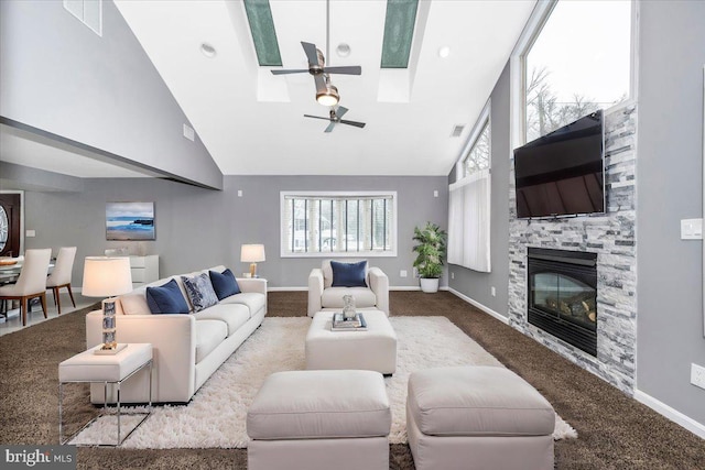 carpeted living room featuring a skylight, ceiling fan, a stone fireplace, and high vaulted ceiling