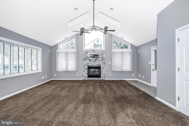 unfurnished living room with dark carpet, vaulted ceiling, ceiling fan, a stone fireplace, and plenty of natural light