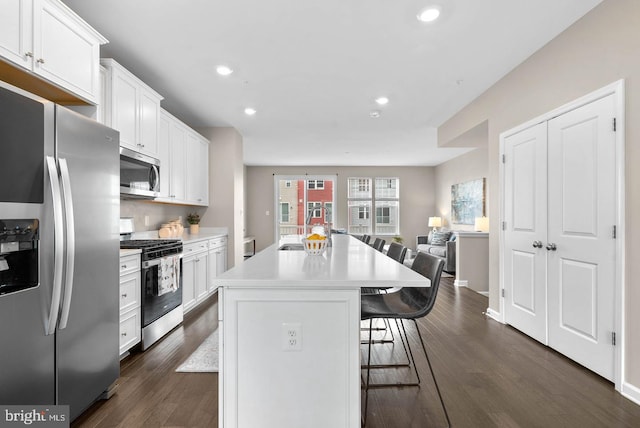 kitchen with white cabinetry, dark hardwood / wood-style floors, a kitchen island, a breakfast bar, and appliances with stainless steel finishes