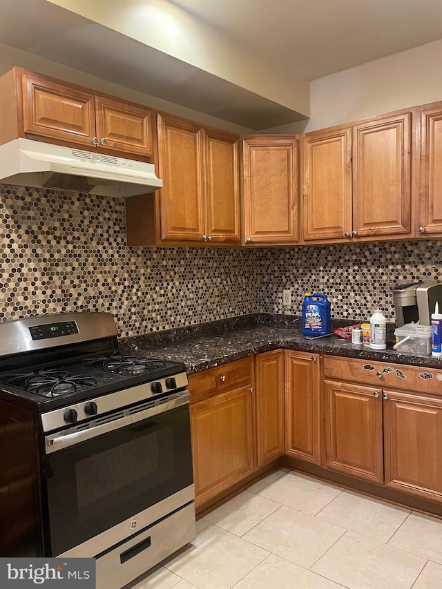 kitchen with decorative backsplash, stainless steel range with gas cooktop, light tile patterned floors, and dark stone counters