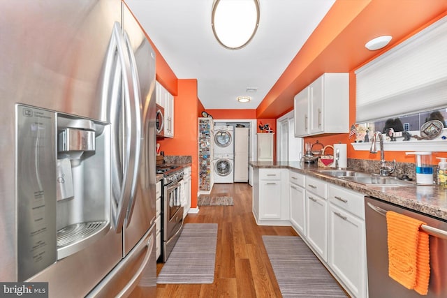 kitchen with stacked washing maching and dryer, appliances with stainless steel finishes, sink, and white cabinets