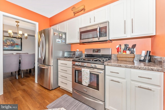 kitchen with pendant lighting, stainless steel appliances, white cabinets, a chandelier, and light wood-type flooring