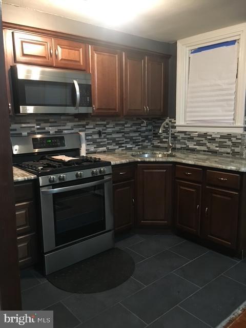 kitchen with tasteful backsplash, sink, dark tile patterned flooring, light stone counters, and stainless steel appliances