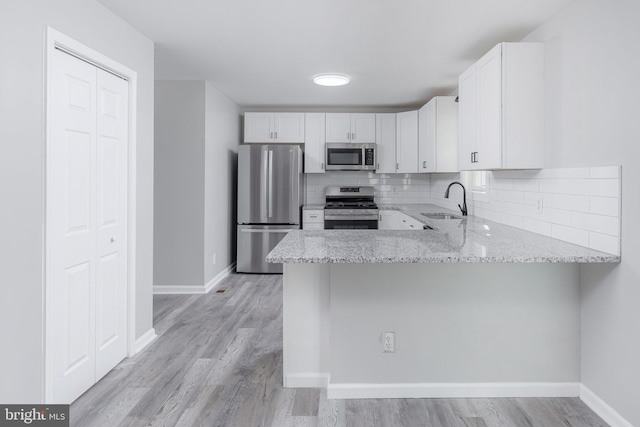 kitchen featuring kitchen peninsula, backsplash, stainless steel appliances, sink, and white cabinets