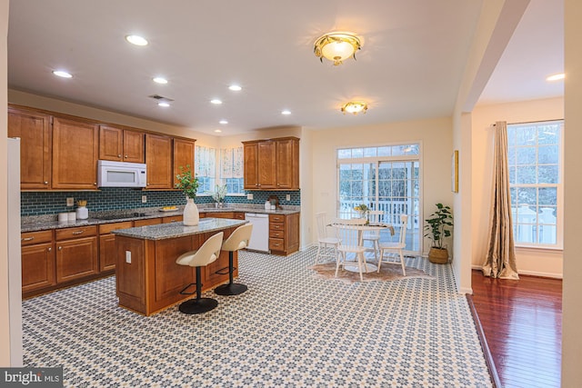 kitchen featuring backsplash, white appliances, a breakfast bar area, and a kitchen island