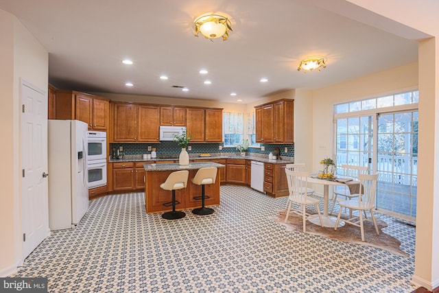 kitchen with a kitchen bar, a center island, tasteful backsplash, white appliances, and sink