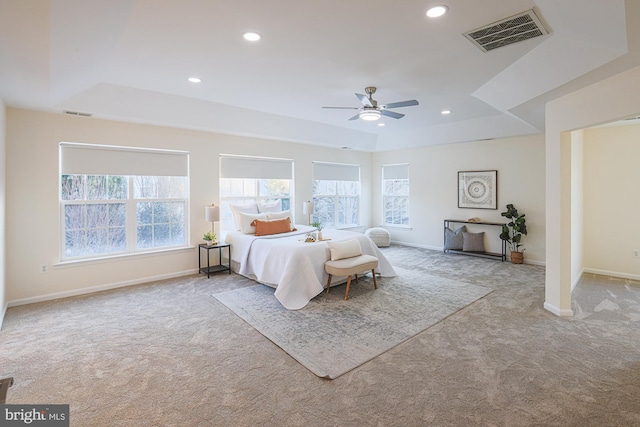 unfurnished bedroom with light carpet, ceiling fan, a tray ceiling, and multiple windows