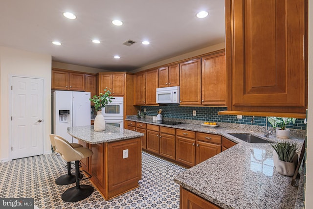 kitchen featuring a kitchen island, a breakfast bar, sink, white appliances, and light stone counters