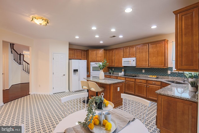 kitchen featuring tasteful backsplash, a center island, sink, white appliances, and light stone countertops